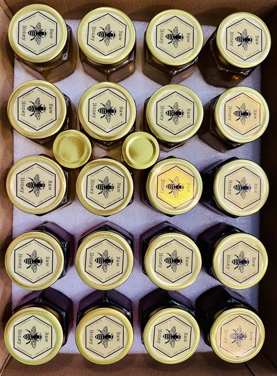 Rows of honey jars from above with gold lids and hexagon Raw Honey labels