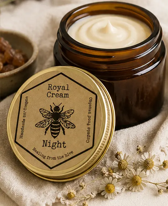 Amber glass jar of white cream beside a gold lid with a kraft hexagon Royal Cream Night label and a bee illustration